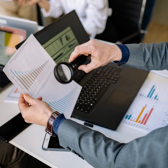 pexels-photo-7793173-7793173 Businessman examines data charts with a magnifying glass over a laptop in an office setting.
